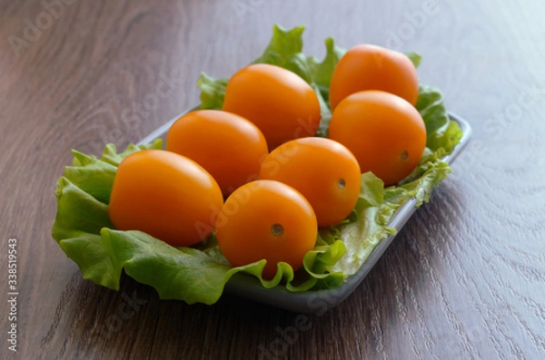 Obraz Yellow cherry tomatoes on a lettuce lie on a plate. Plate is on a wooden tabletop.