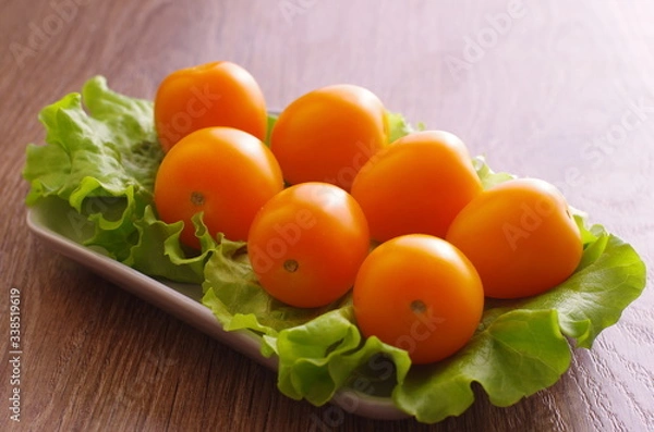 Obraz Yellow cherry tomatoes on a lettuce lie on a plate. Plate is on a wooden tabletop.