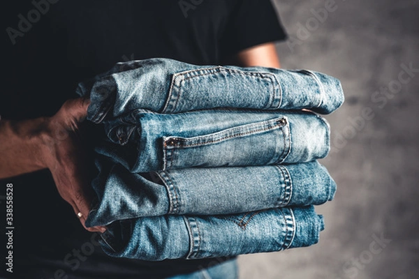 Fototapeta close up stack of folded denim blue jeans in hand over gray wall background, copy space