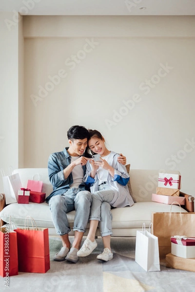 Fototapeta Young Asian couple at home using a smartphone