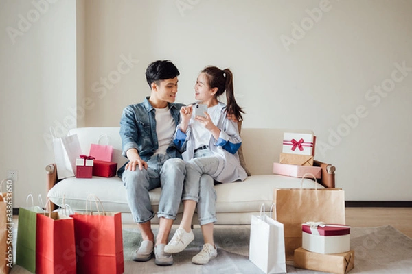 Fototapeta Young Asian couple at home using a smartphone