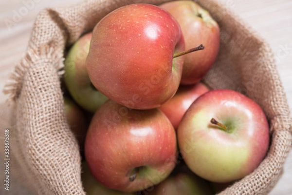 Fototapeta Bag with apples. Studio image. Red apples in a burlap bag on a wooden background. Fabric bag full of apples.