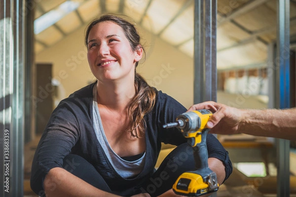 Fototapeta Young cute caucasian woman with black hair is being offered a work tool and she is kindly refusing it. Woman refusing to work with home tools.