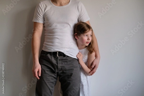 Obraz scared little girl hiding behind her dad. Daughter seeks protection from a man