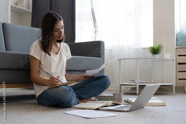 Fototapeta Coronavirus. Beautiful young smiling woman in quarantine working on laptop from home.