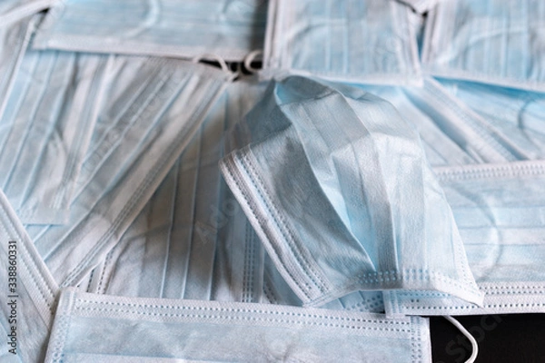 Obraz Protective masks on black background. A used surgical mask on a bed of unused surgical masks. Medical PPE.