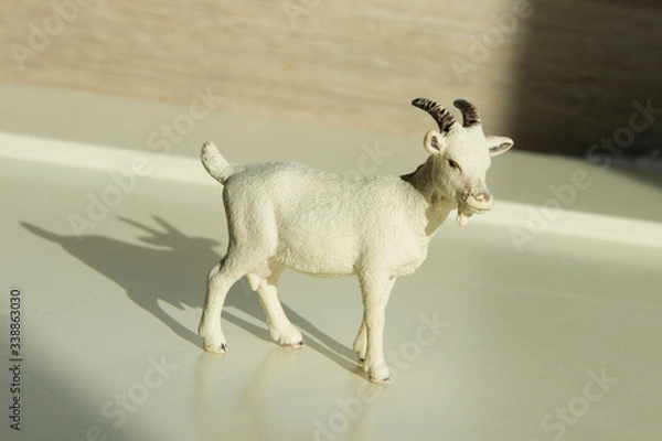 Fototapeta very small toy plastic kid, goatling with shadow on a wooden table