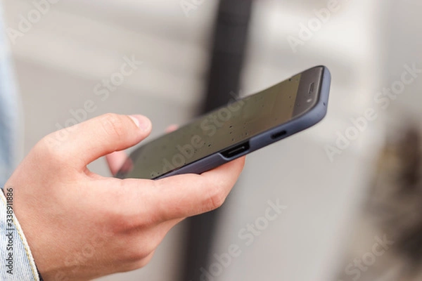 Obraz man holding a phone. mobile phone in a man's hand. checking a phone. sending messages. man reading news on a smartphone