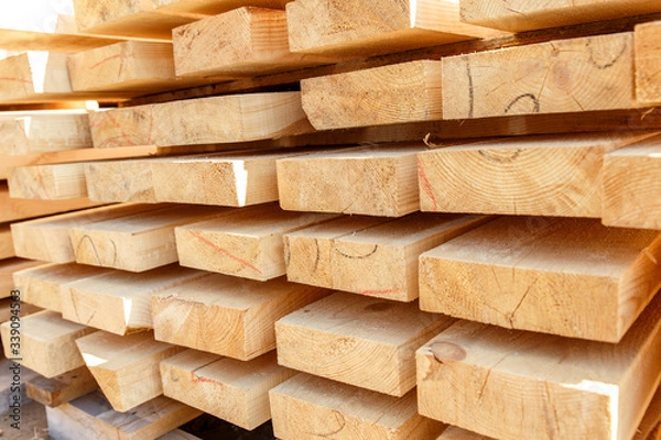 Fototapeta Stack of new wooden studs at the lumber yard. Timber on the construction site to dry. Background of sawed and processed wood of coniferous breeds.