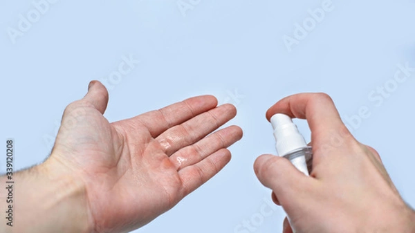 Obraz A man sprays a disinfectant on his hands against infection with coronavirus during quarantine. Isolated on a gray background in the studio. Coronavirus concept
