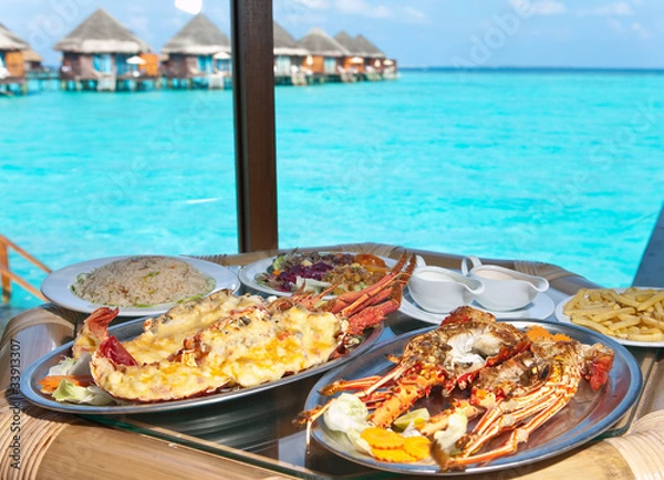 Obraz Two plates with lobster on table at window with view on ocean..
