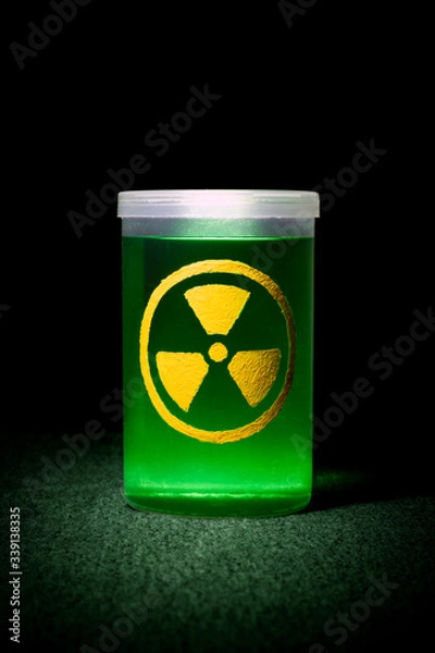 Obraz glowing toxic radioactive waste in a transparent cylindrical container with yellow sign on a black background