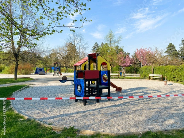 Fototapeta Children's playground in the park is closed and wrapped in alarm caution tape for global coronavirus quarantine. No children on playgrounds in Europe. Prevention of coronavirus COVID-19.