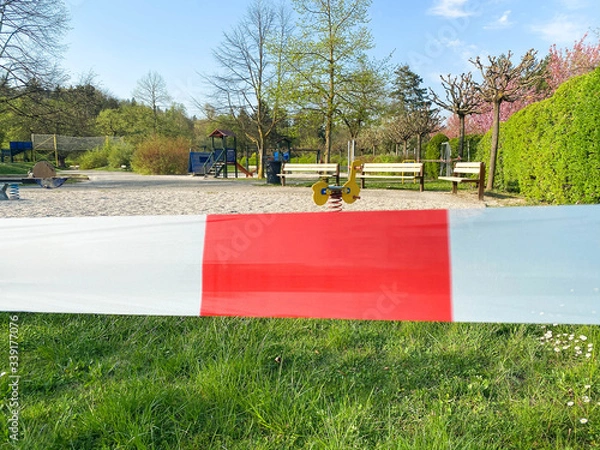 Fototapeta Children's playground in the park is closed and wrapped in alarm caution tape for global coronavirus quarantine. No children on playgrounds in Europe. Prevention of coronavirus COVID-19.