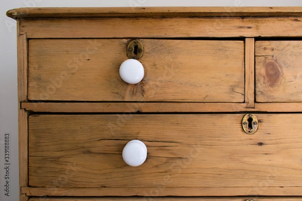 Fototapeta Antique Victorian wooden chest of drawers with crisp white ceramic knobs for handles with traditional brass key hole locks in each drawer