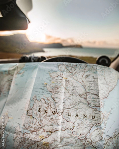 Fototapeta Planning a Road Trip adventure around Scotland with a map in hands parked overlooking the sunset