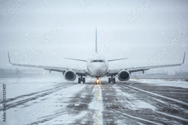 Fototapeta Airliner on runway in blizzard. Aircraft during taxiing during heavy snow. Passenger plane in snow at airport. Passenger airplane taxiing for take off at airport during snow blizzard