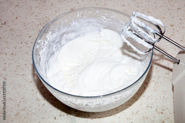 Fototapeta making whipped cream with a mixer in the kitchen