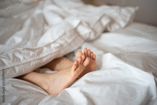 Obraz Female feet peeking out from white blanket