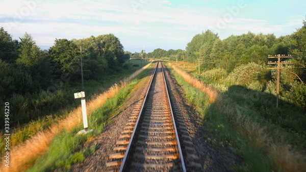 Fototapeta Back view of railroad and a beautiful green nature from a train passing on countryside land. Railroad travel or railway tourism concept. Slow motion back view 4K video.