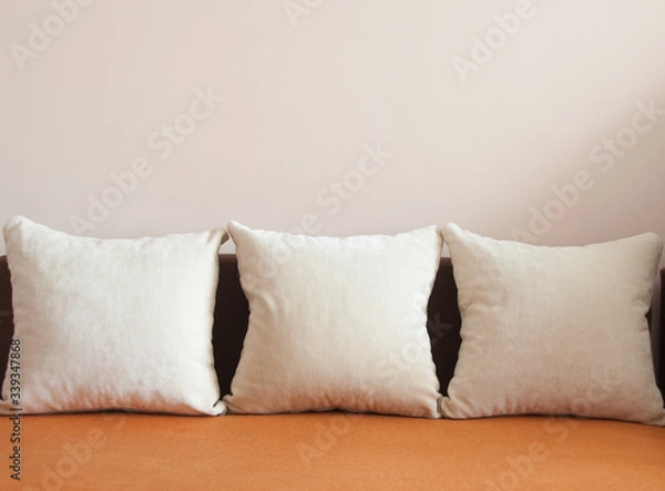 Fototapeta Orange fabric sofa with three white pillows. Pink background. Home concept. Copy space