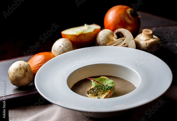 Fototapeta Mushroom soup in white bowl on a black background.On the table are mushrooms and onions.