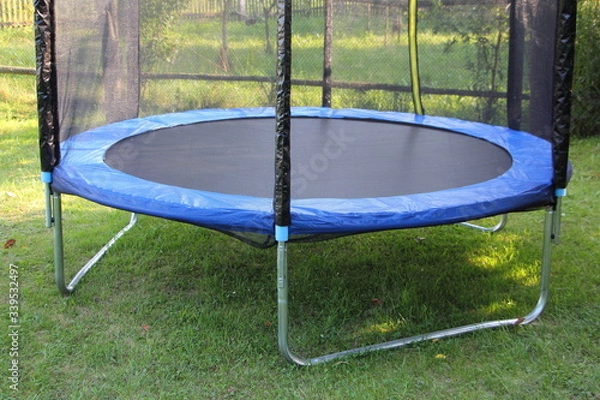 Fototapeta Modern empty 8ft trampoline with outside pritection net on green grass on a summer day close-up, fitness outdoor training