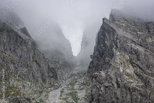 Fototapeta Mountain pass surrounded by fog, grey rocks in the mountains, passage between the peaks, invisible due to low clouds, in Tatra Mountains