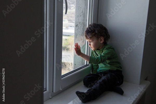 Fototapeta the child misses walks on the street and fresh air sitting on the windowsill by the window.