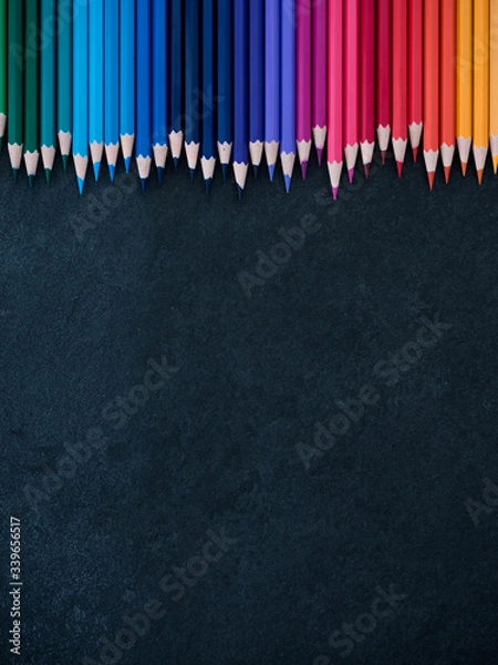 Fototapeta Set of colored pencils arranged in a row on slate background