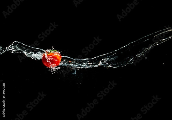 Fototapeta Fresh ripe red tomato with green leave flying in wave of water in the air isolated on black background. Concept of food levitation