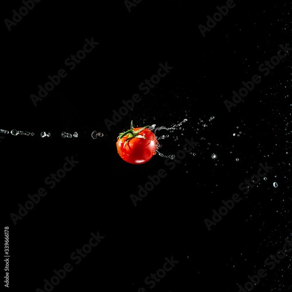 Fototapeta A fresh ripe red tomato with a green leaf flies in the air in water drops isolated on a black background. Concept of food levitation