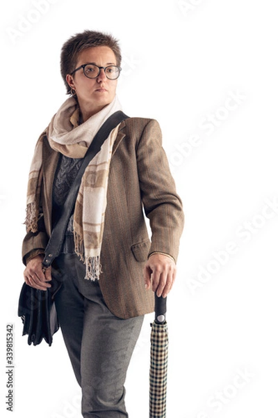Fototapeta A woman with a short haircut, in a light jacket and with a light scarf around her neck, with a bag posing on a white background in the studio. Copy space.
