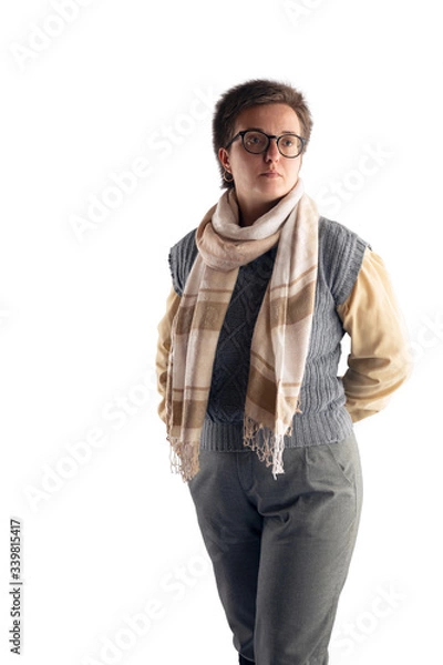 Fototapeta A woman with glasses and a short haircut, in a gray knitted vest, in a shirt and with a scarf around her neck poses on a white background in the studio.