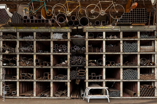 Fototapeta Different styles and sizes of old recycled metal pipes and profiles construction materials laying on a shelf rack in a storage. Recycled metal pieces, circular economy principle