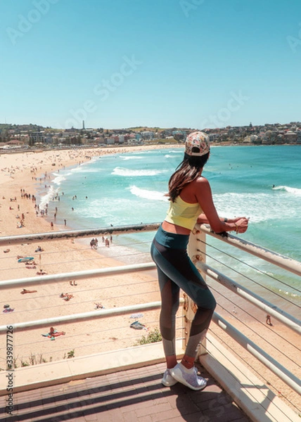Fototapeta Woman at Bondi Beach, Sydney, Australia. Girl in work out gear looking at view of the ocean, sun, sea and sand scene, while on vacation. Holiday, tropical, fitness concepts. 