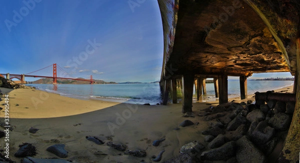 Fototapeta Golden Gate Bridge unique perspective from under wharf with nice sun reflection on concrete.