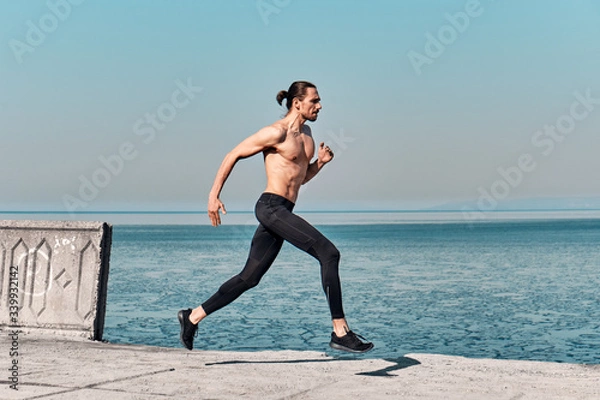Obraz Side view of Topless Healthy Handsome Active Man running on sidewalk in morning At Sea. Health conscious concept with copy space.