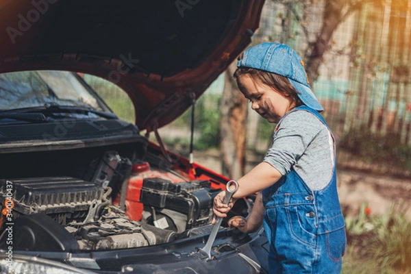 Fototapeta Little child trying to fix broken real car. Dreaming to be auto technician