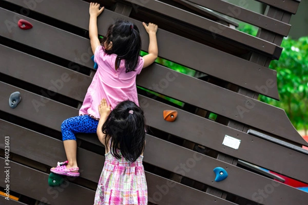 Fototapeta Pretty asian little twins girls while climbing in a playground and helping each other