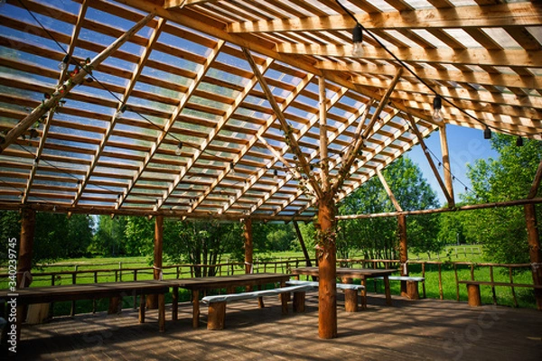 Fototapeta Wooden gazebo in nature in the Park for events. Sunlight through a grid of wooden beams-a game of chiaroscuro. Place for text and background