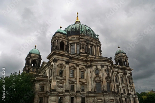 Fototapeta View of the upper part of the cupola of the Berlin Cathedral with the turquoise copper roof and golden cross on top in front of an impressive sky with white grey clouds; Berlin, Germany, Europe
