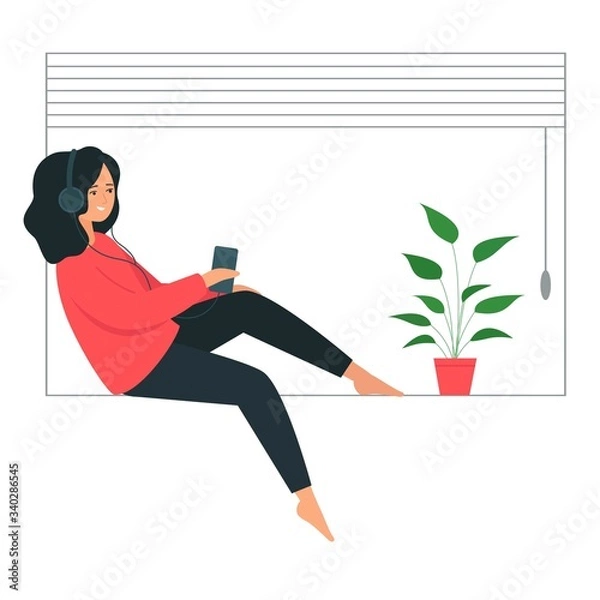 Obraz The girl in the headphones sits on the windowsill. A young woman holds a smartphone in her hand and listens to music.