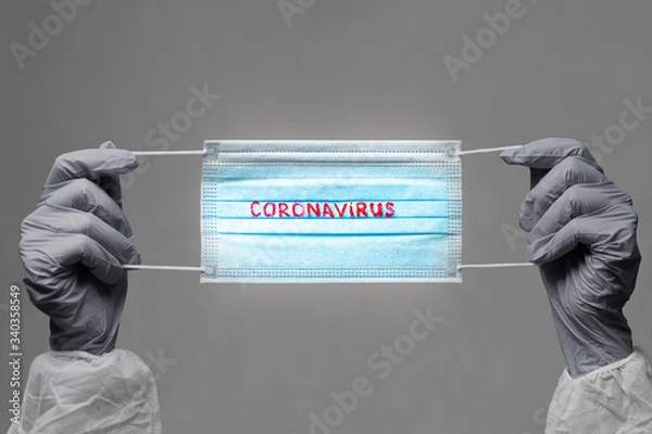 Obraz CORONAVIRUS. COVID-19 concept. blue medical face mask with a red inscription CORONAVIRUS in the hands of which are in rubber gloves. vignette image