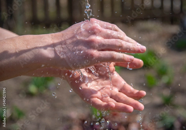 Obraz Strong male hands under a stream of water on a blurred natural background.