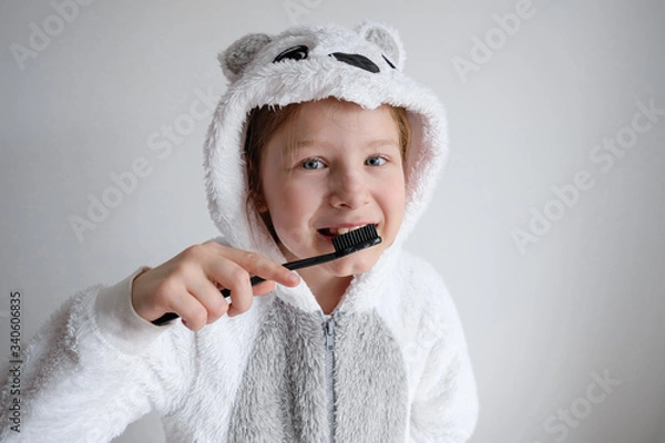 Obraz the little girl woke up in the morning and brushes her teeth with black coal toothpaste. The girl is wearing pajamas in the animal