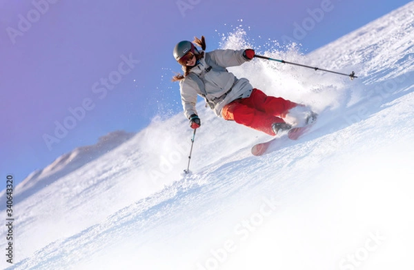 Obraz Girl On the Ski. a skier in a bright suit and outfit with long pigtails on her head rides on the track with swirls of fresh snow. Active winter holidays, skiing downhill in sunny day. Woman skier