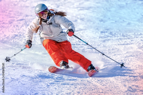 Obraz Girl On the Ski. a skier in a bright suit and outfit with long pigtails on her head rides on the track with swirls of fresh snow. Active winter holidays, skiing downhill in sunny day. Woman skier