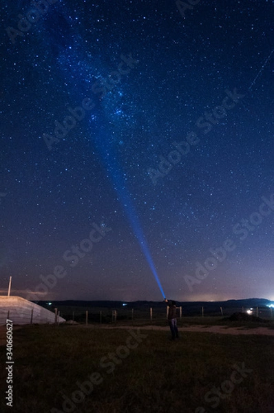 Fototapeta milky way sky with a silhouette man flashing a lantern to the sky