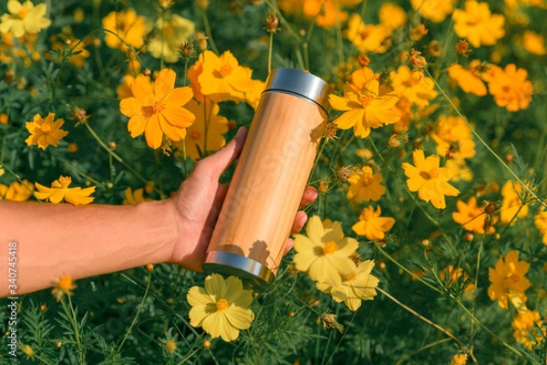 Obraz Hand holding wood pattern stanless bottle with cosmos flower as background. Zero waste concept. safe the world concept.